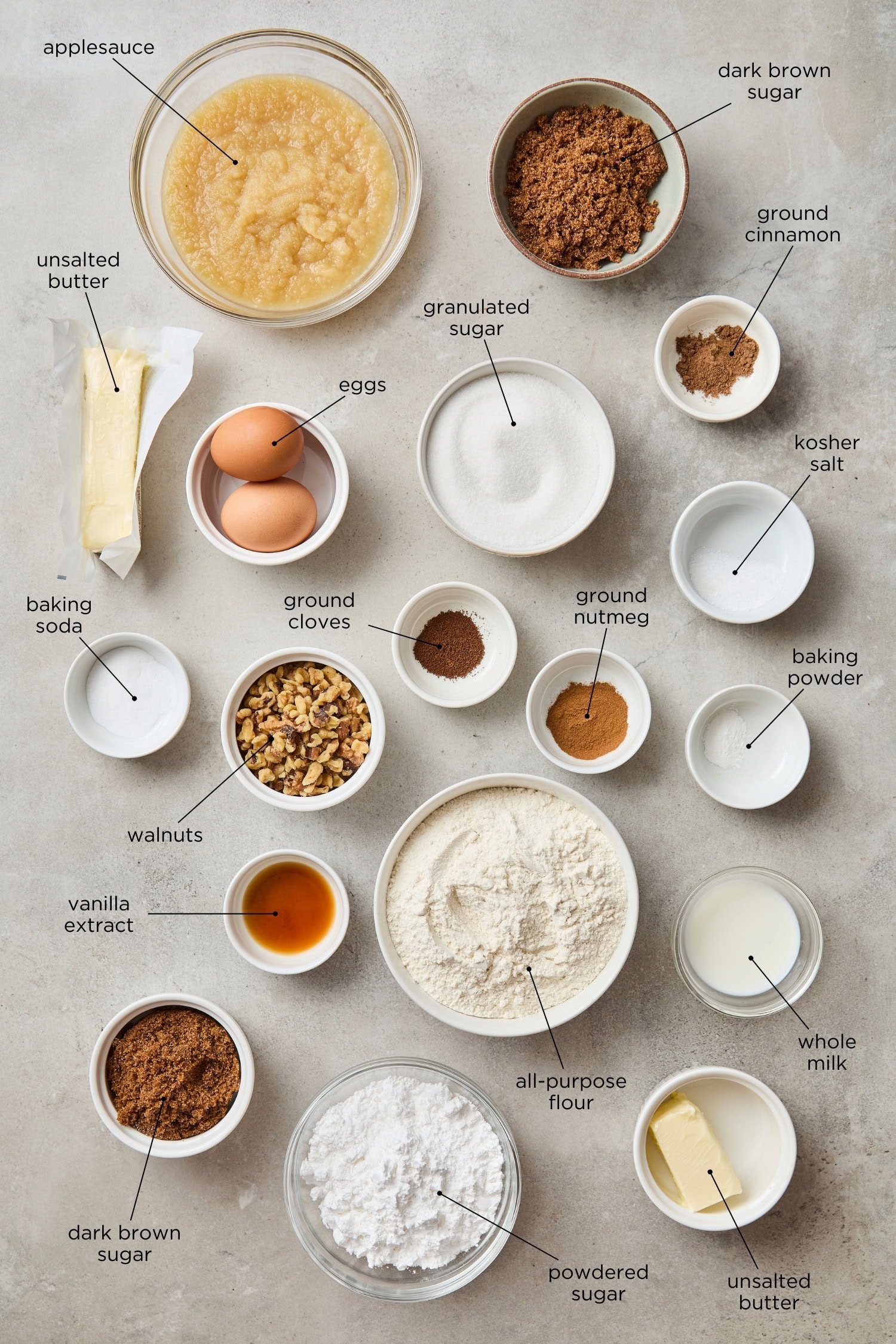 Concrete surface with ingredients needed for applesauce cake including flour, sugar, butter, spices, and more.