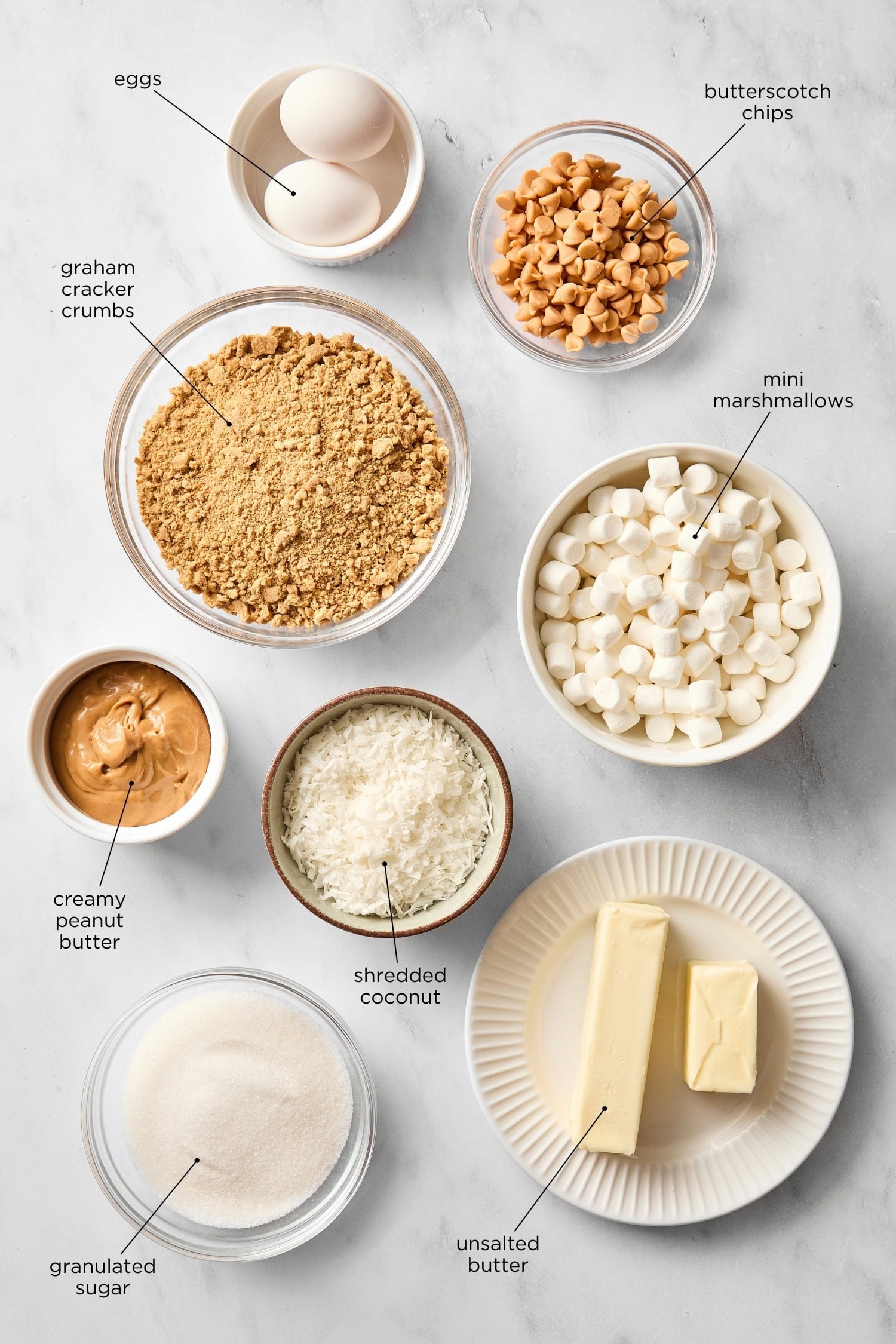 White marble surface filled with ingredients for butterscotch bars including chips, marshmallows, butter, and more.