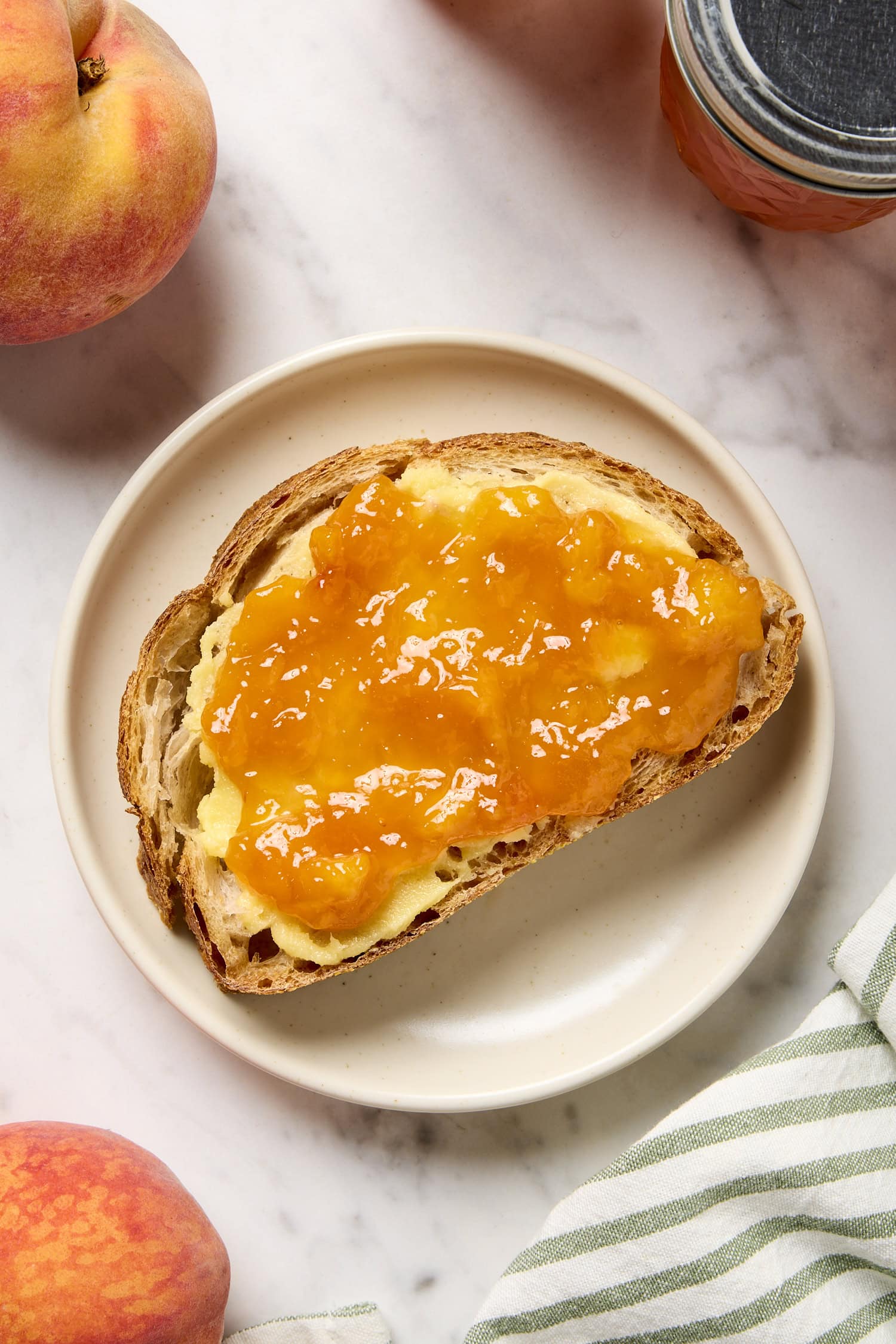 A piece of toast with peach jam and butter on a plate.