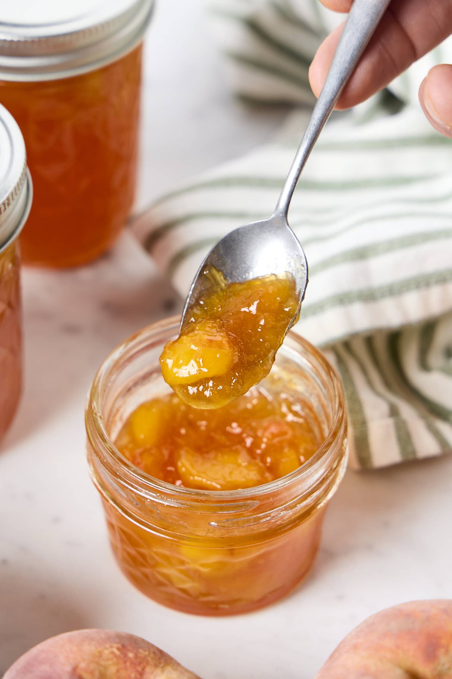 Spooning peach jam out of a jar.