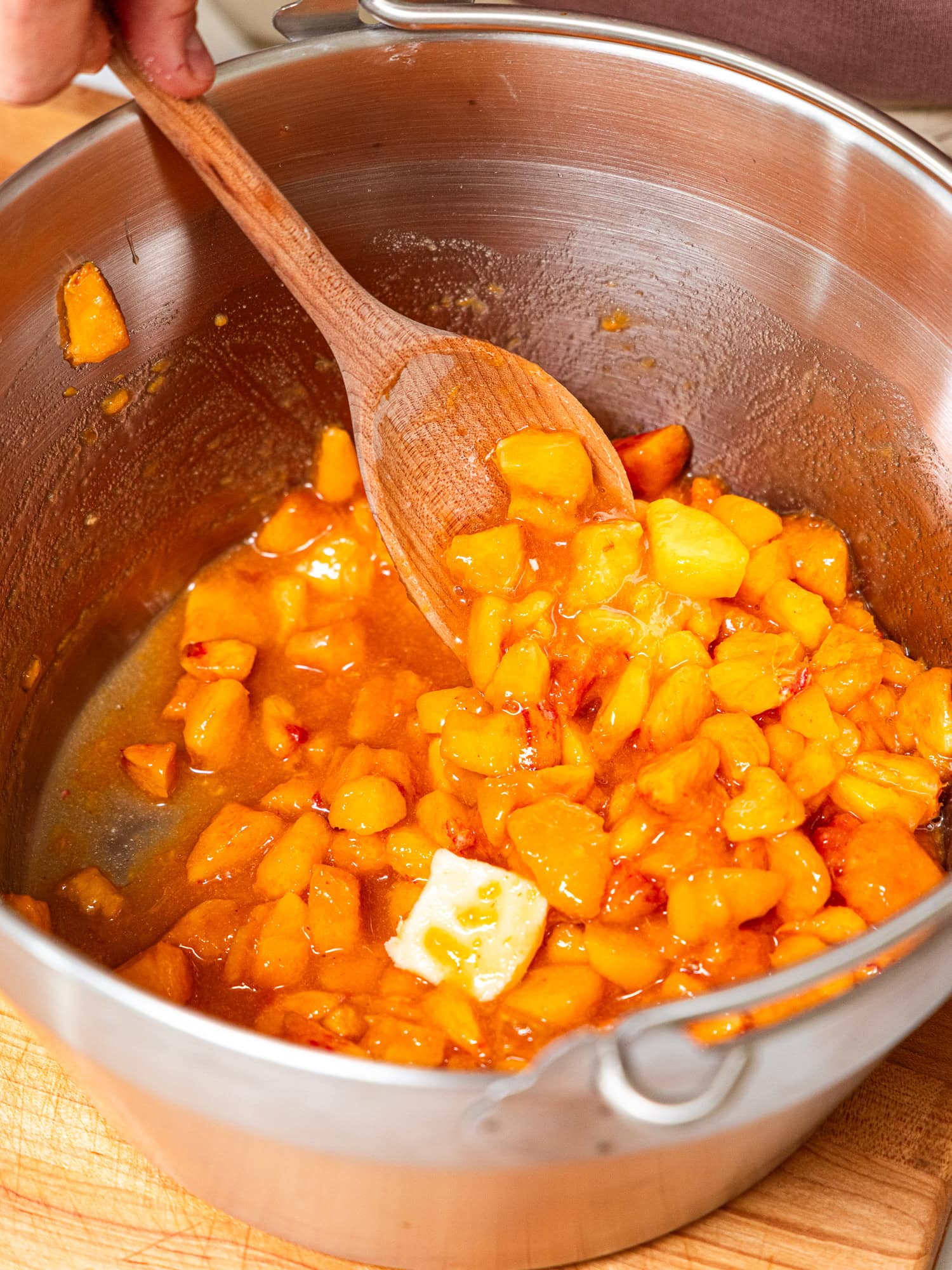 Stirring in peach chunks, sugar, lemon juice, and butter before cooking into a jam.