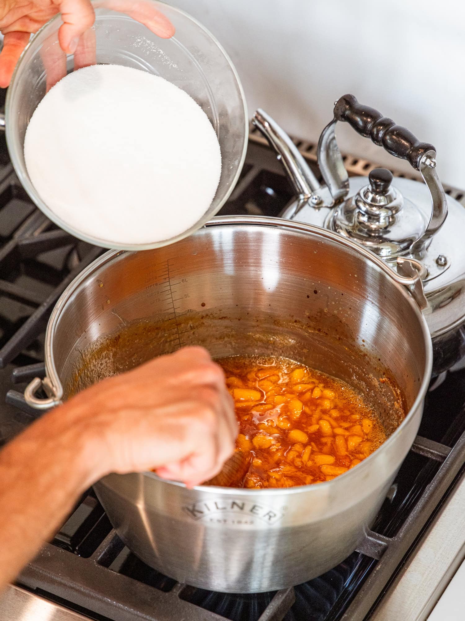 Adding additional sugar while cooking peach jam.