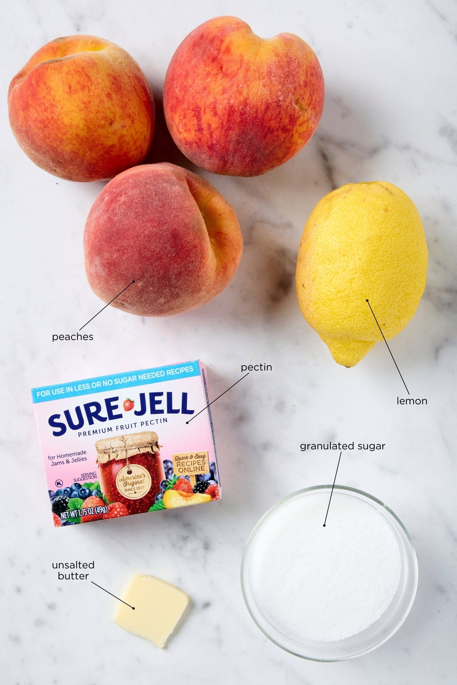 Ingredients to make peach jam including peaches, sugar, lemon, pectin, and unsalted butter.