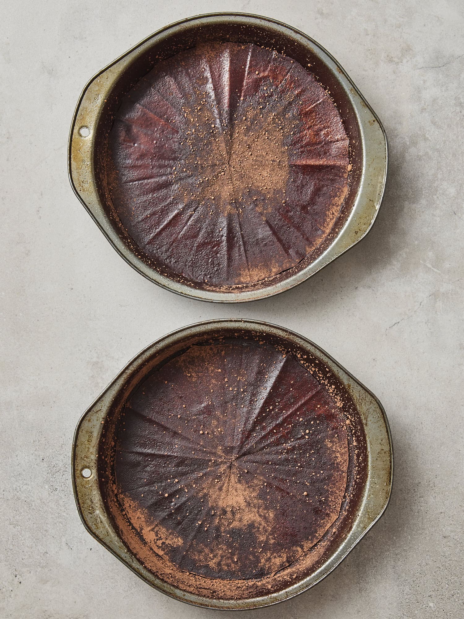 Two pans filled with parchment rounds and dusted with cocoa powder.