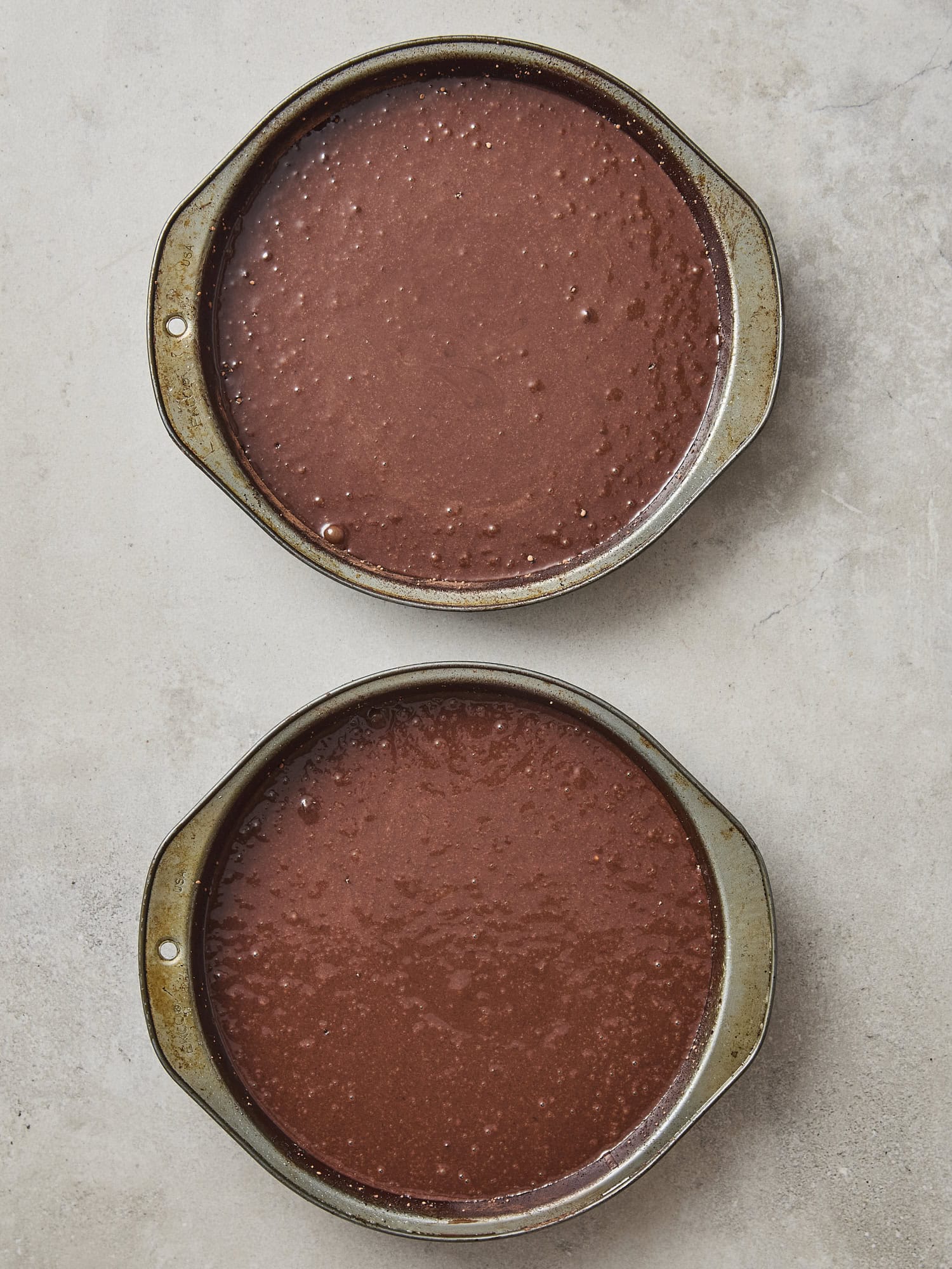 Two cake pans filled with chocolate cake batter before going in the oven.