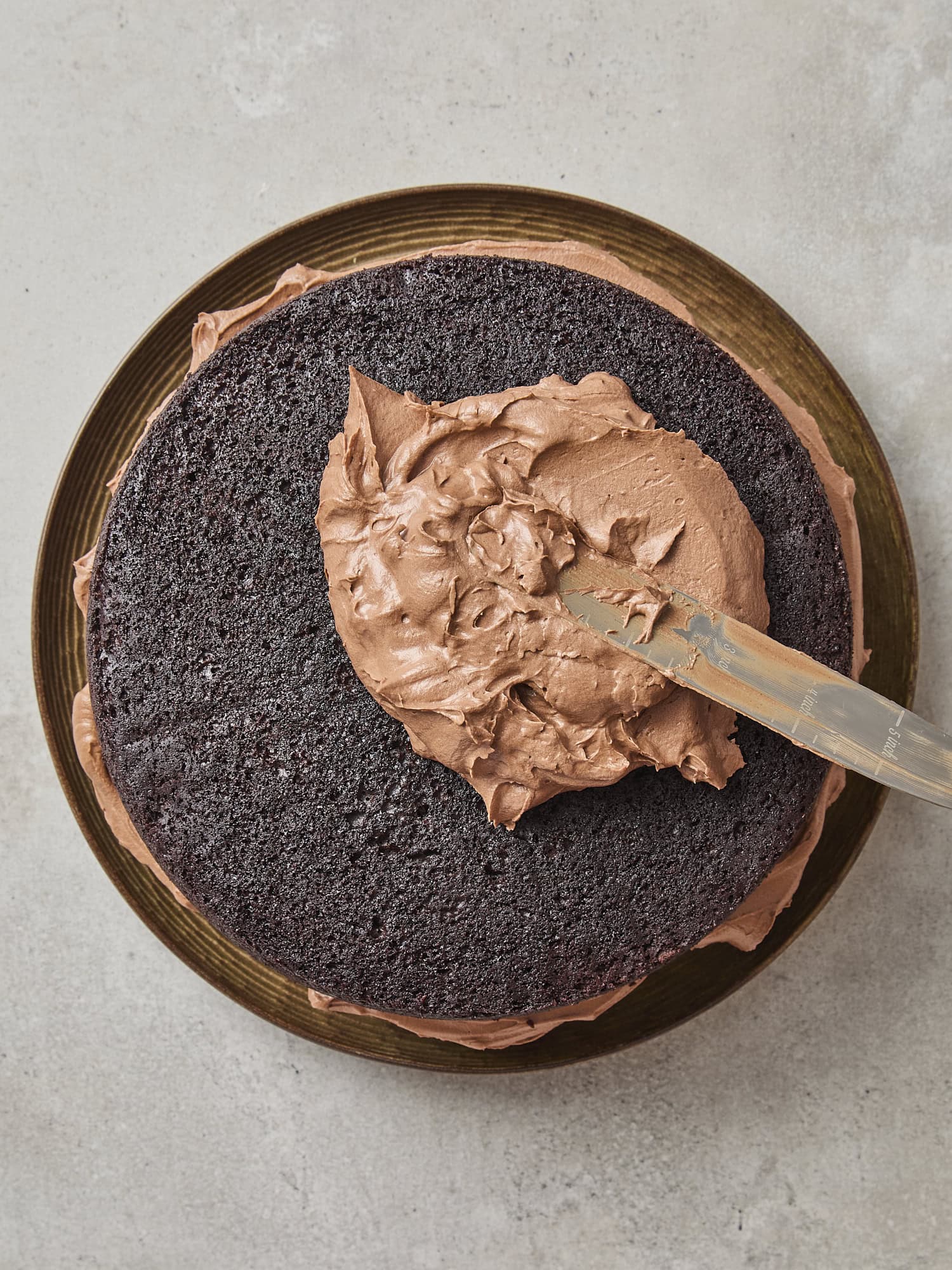 Chocolate cake round being frosted showing dark chocolate texture.