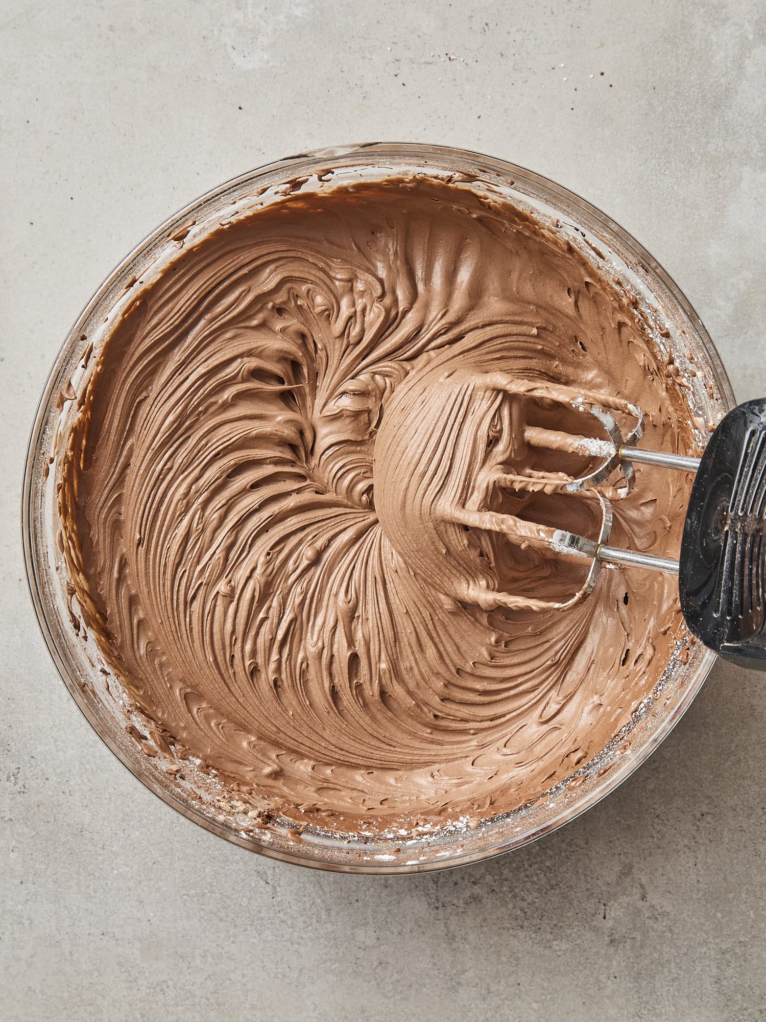 Mixer in a bowl making chocolate frosting with swirled texture.