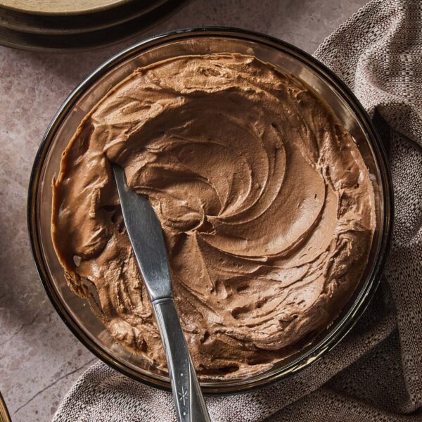 Bowl filled with swirled chocolate frosting with knife ready to spread more.