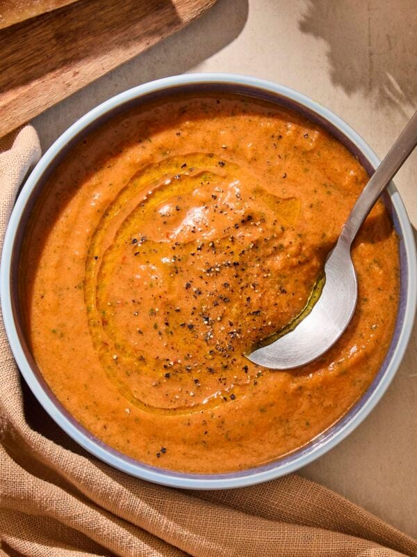 Bowl of gazpacho soup with black pepper sprinkled on top and spoon scooping a serving.