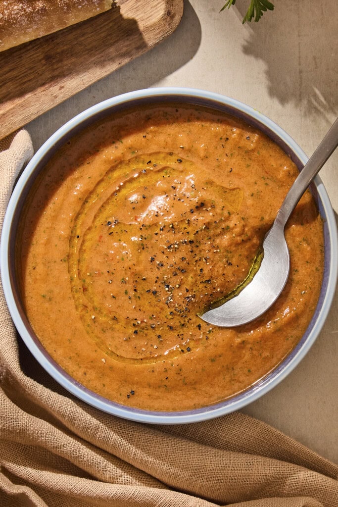 Bowl of gazpacho soup with black pepper sprinkled on top and spoon scooping a serving.