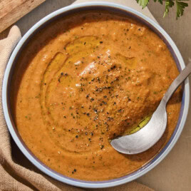Blue bowl with creamy gazpacho soup inside with spoon.