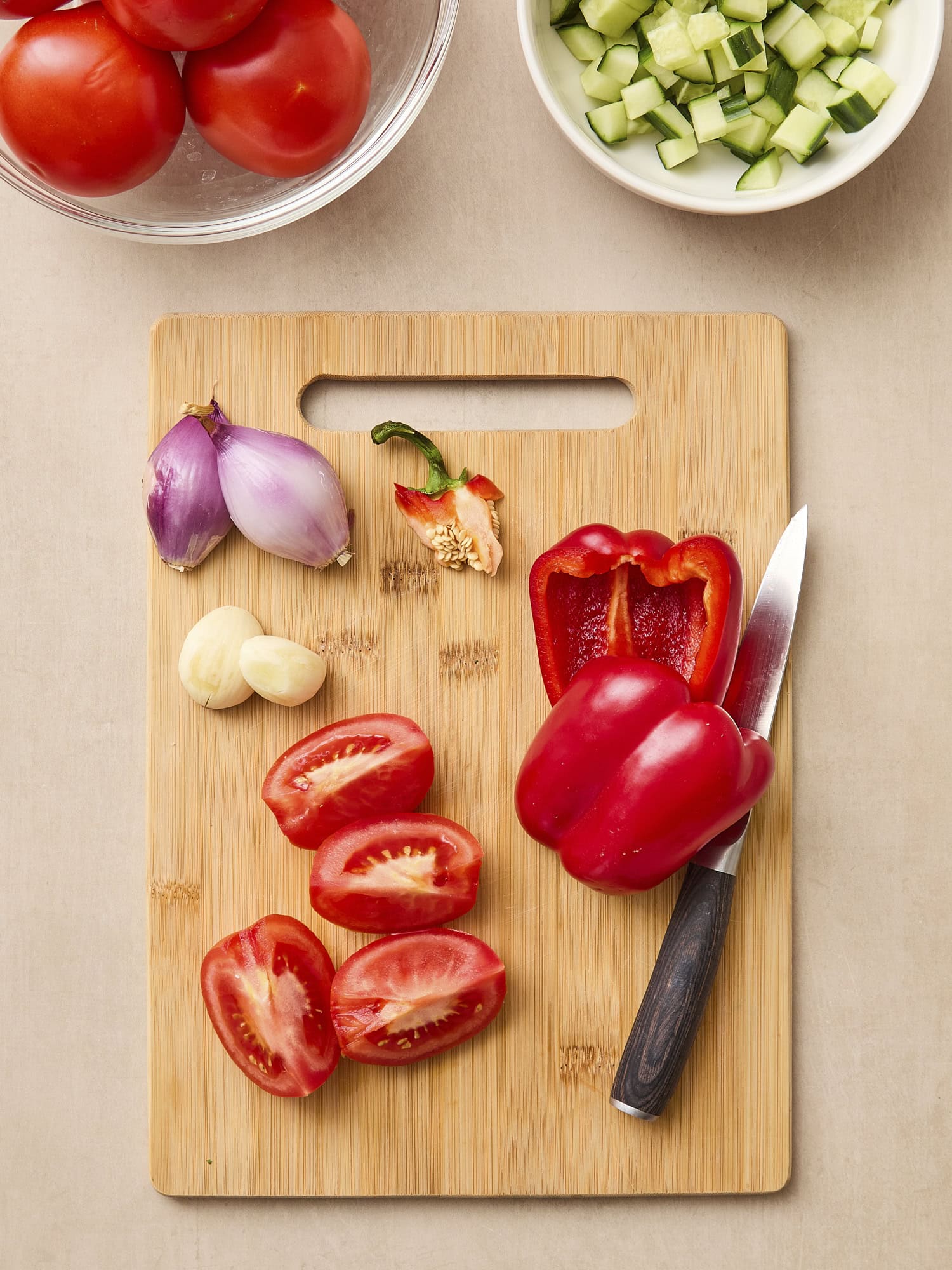 Cutting board with tomatoes and red bell pepper being prepared for soup.