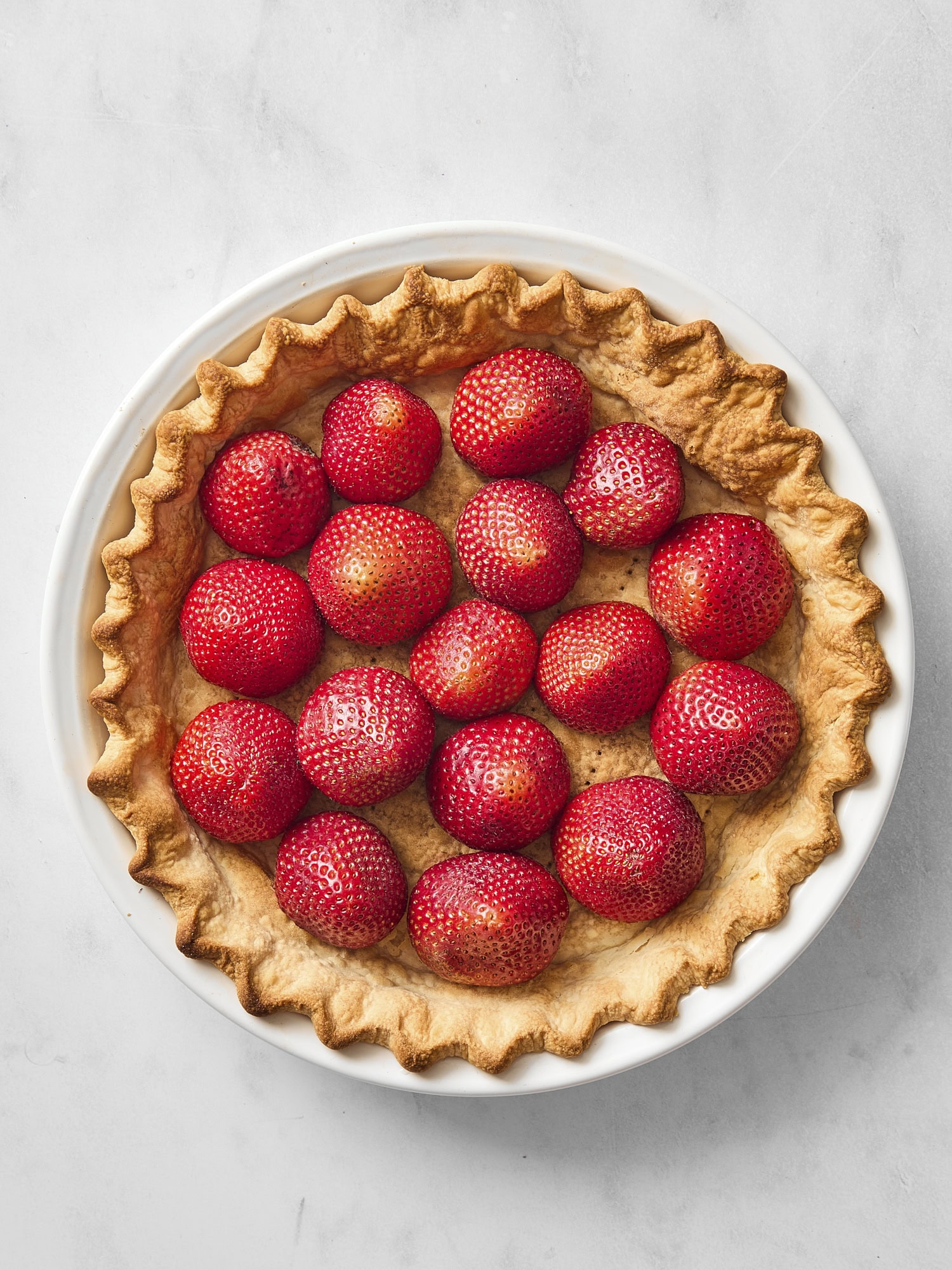 Baked crust for a pie with strawberries lined up inside.