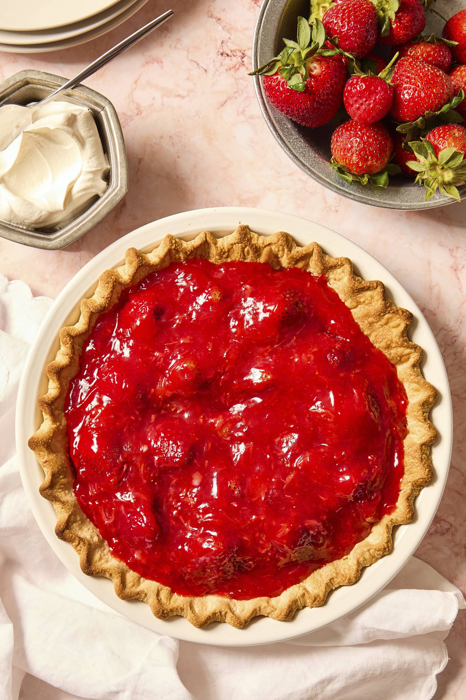 Baked strawberry pie with more strawberries and whipped cream to the side.