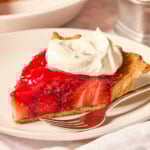 White plate with slice of fresh strawberry pie with whipped cream on top.