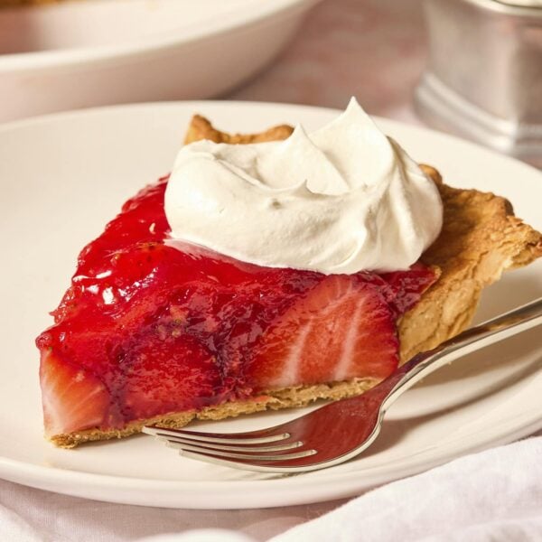 White plate with slice of fresh strawberry pie with whipped cream on top.
