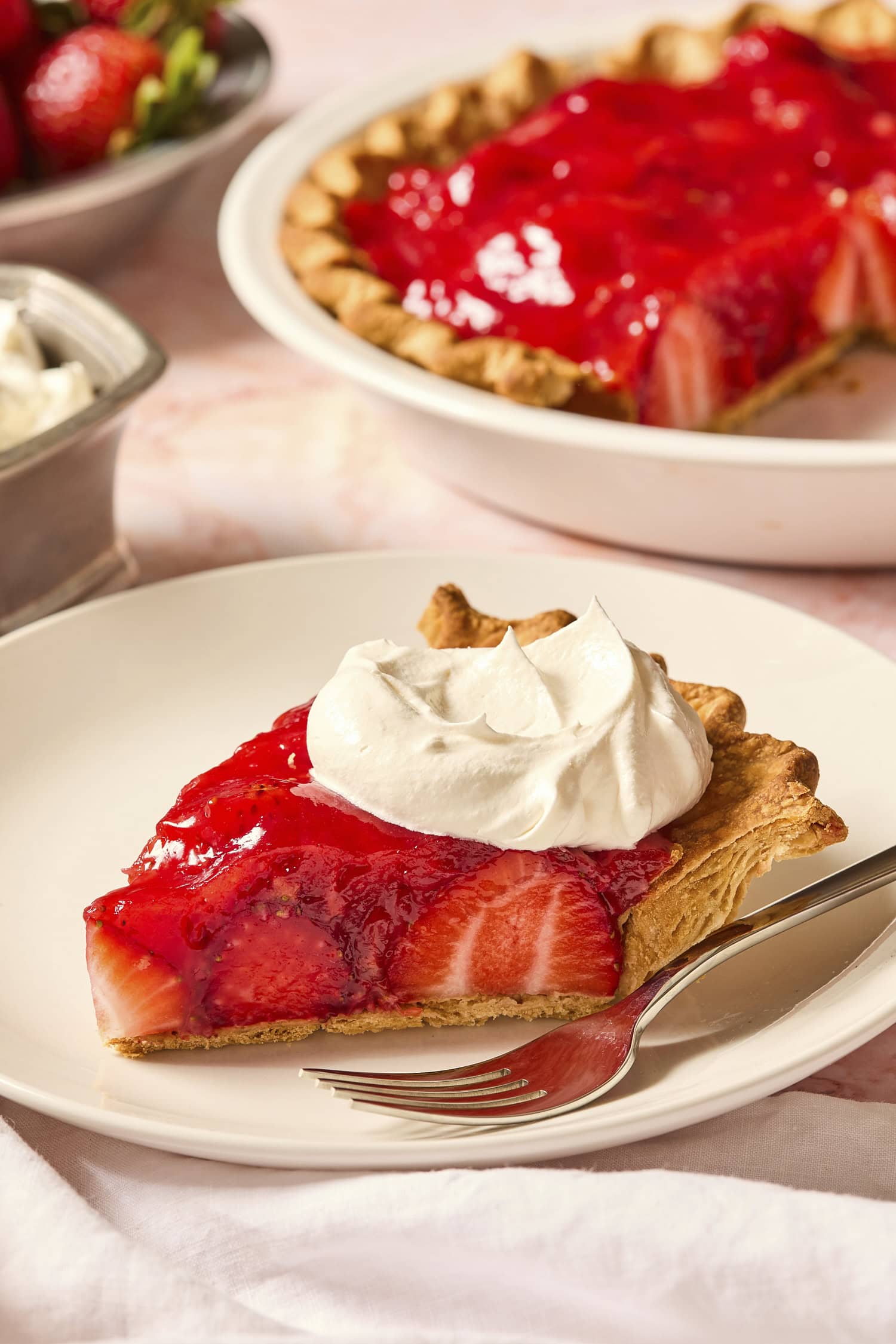 Piece of strawberry pie with whipped cream on top on a plate after being sliced.