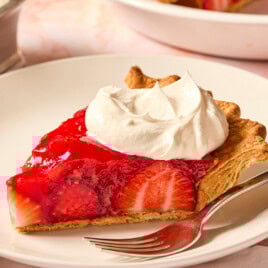 Piece of strawberry pie on a white plate with dollop of whipped cream on top.