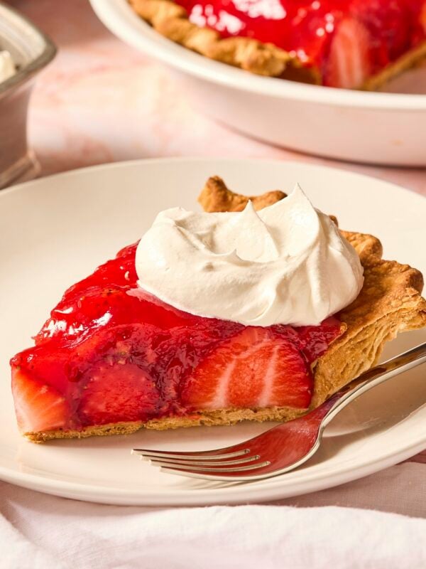 Piece of strawberry pie on a white plate with dollop of whipped cream on top.