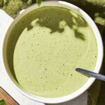 Bowl filled with green colored salad dressing for a salad with a spoon in bowl.