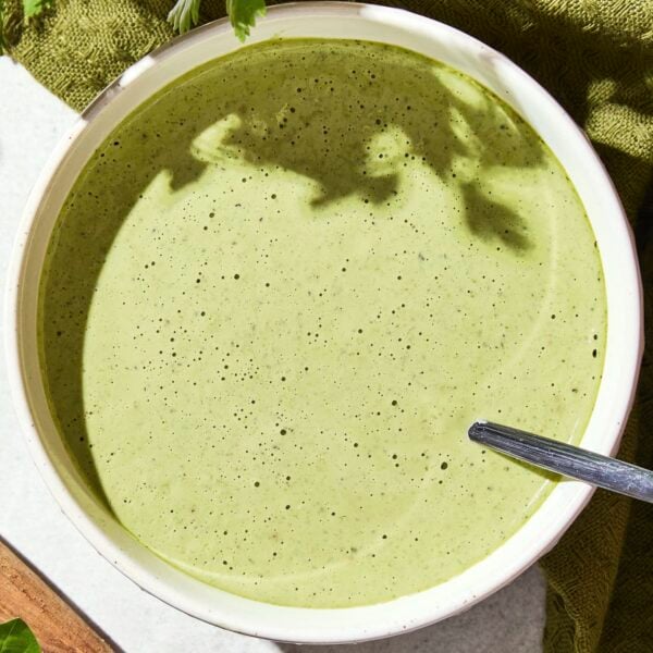 Bowl filled with green colored salad dressing for a salad with a spoon in bowl.
