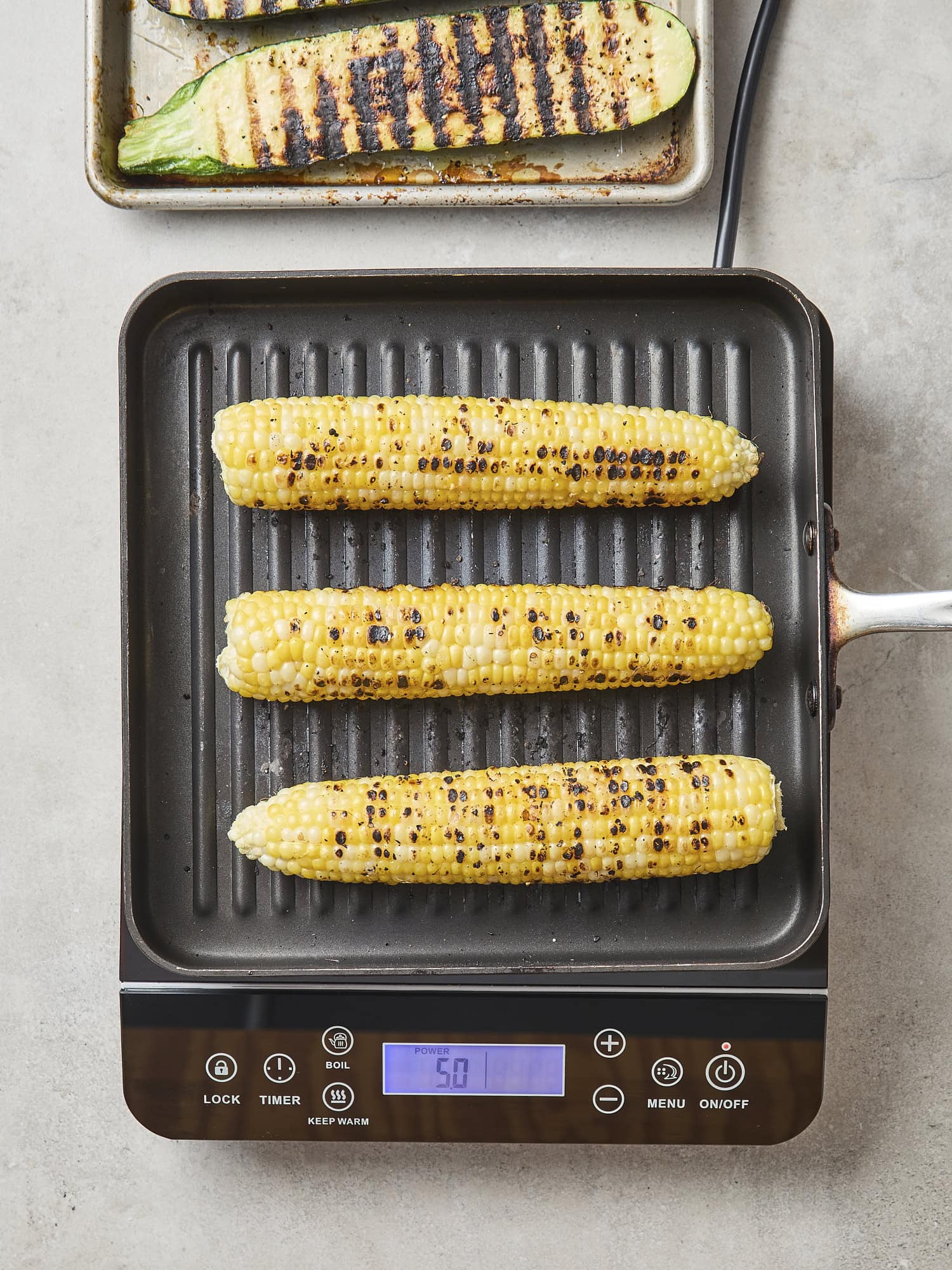 Grill pan on counter with sweet corn being grilled with char marks.