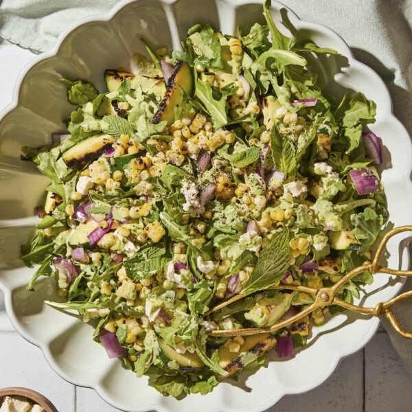 Large salad bowl filled with grilled sweet corn salad with red onions, zucchini, and dressing.