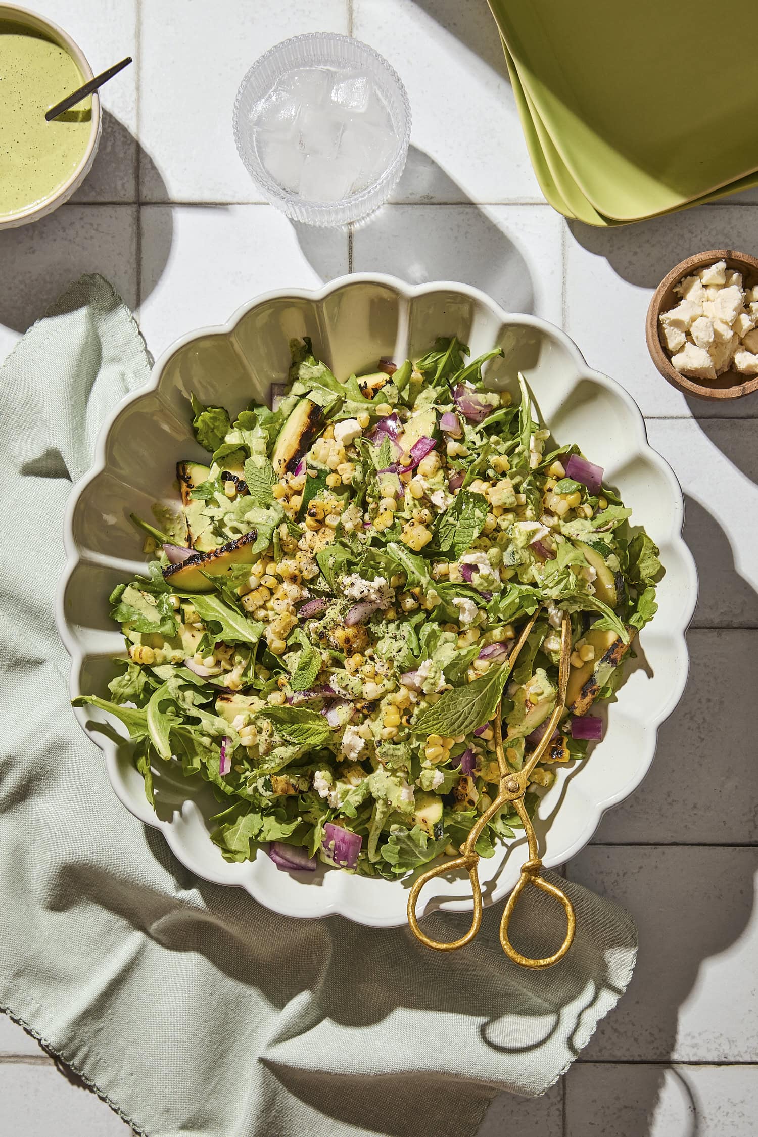Big salad bowl filled with sweet corn salad topped with zucchini, red onion, and dressing.