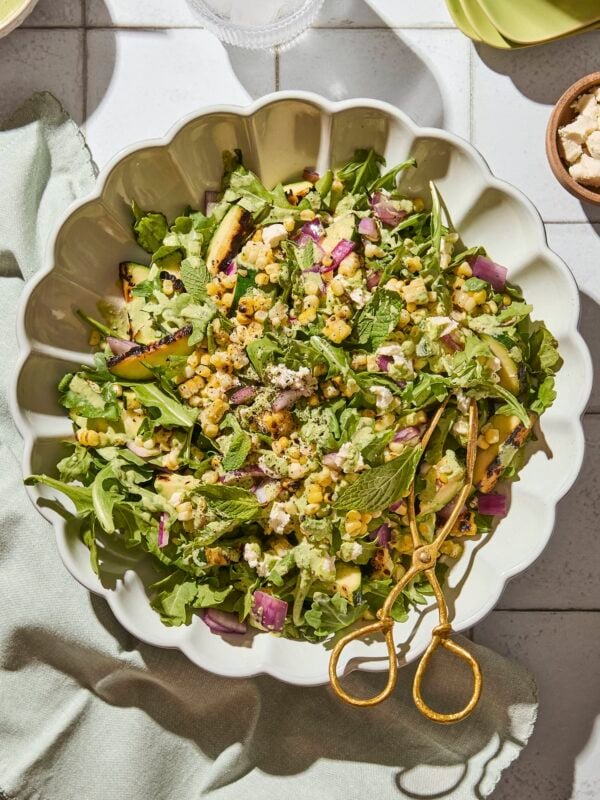 White bowl filled with grilled sweet corn salad with zucchini and red onion all on arugula.