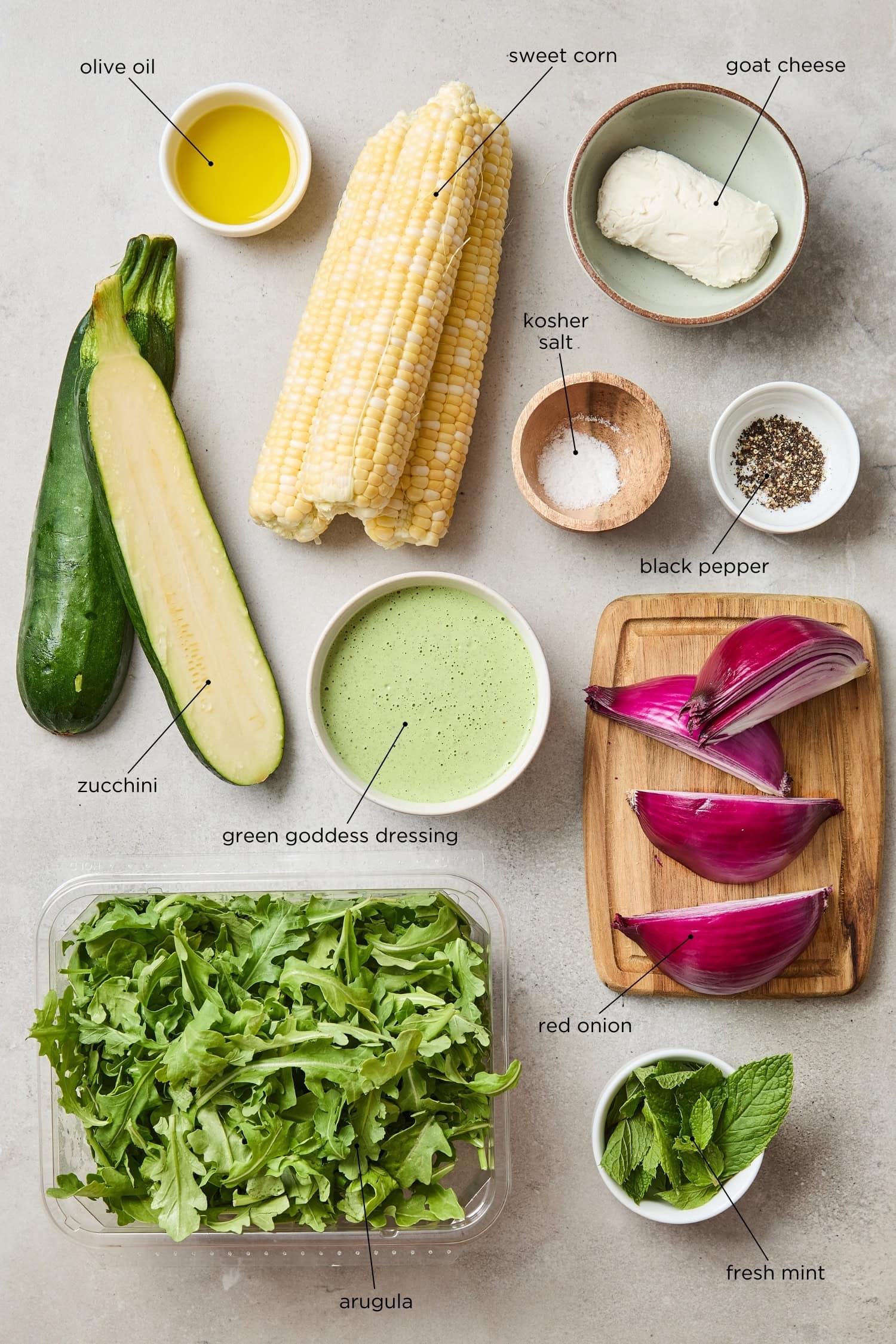 Surface with ingredients for a grilled sweet corn salad including zucchini, arugula, sweet corn, and more.