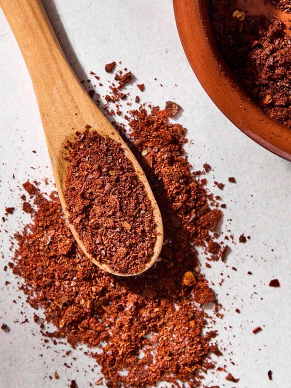 Spoon filled with reddish homemade chili powder with some spilling.