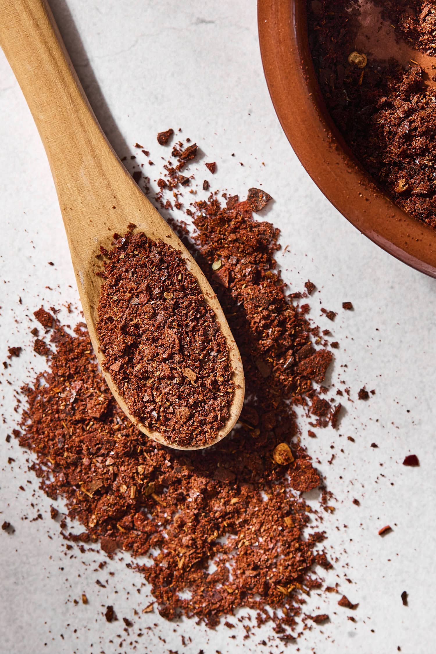 Spoon filled with reddish homemade chili powder with some spilling.
