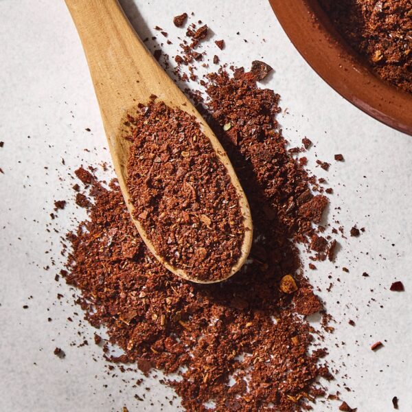 Concrete surface with homemade chili powder with reddish color on a spoon.