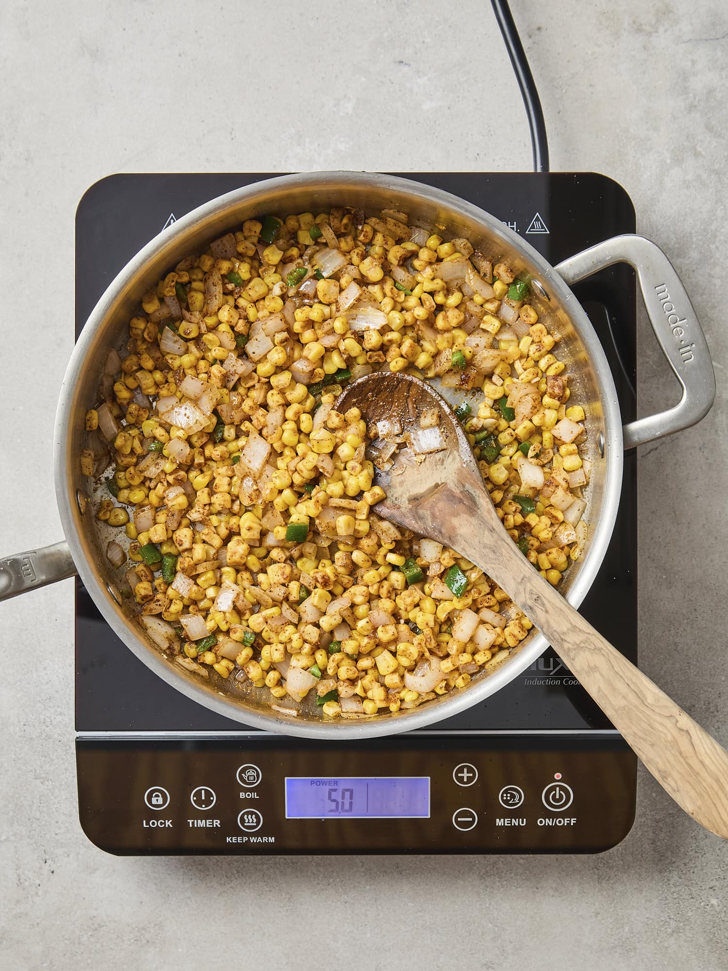 Hot plate with pan filled with cooking sweet corn with onion and jalapeno.