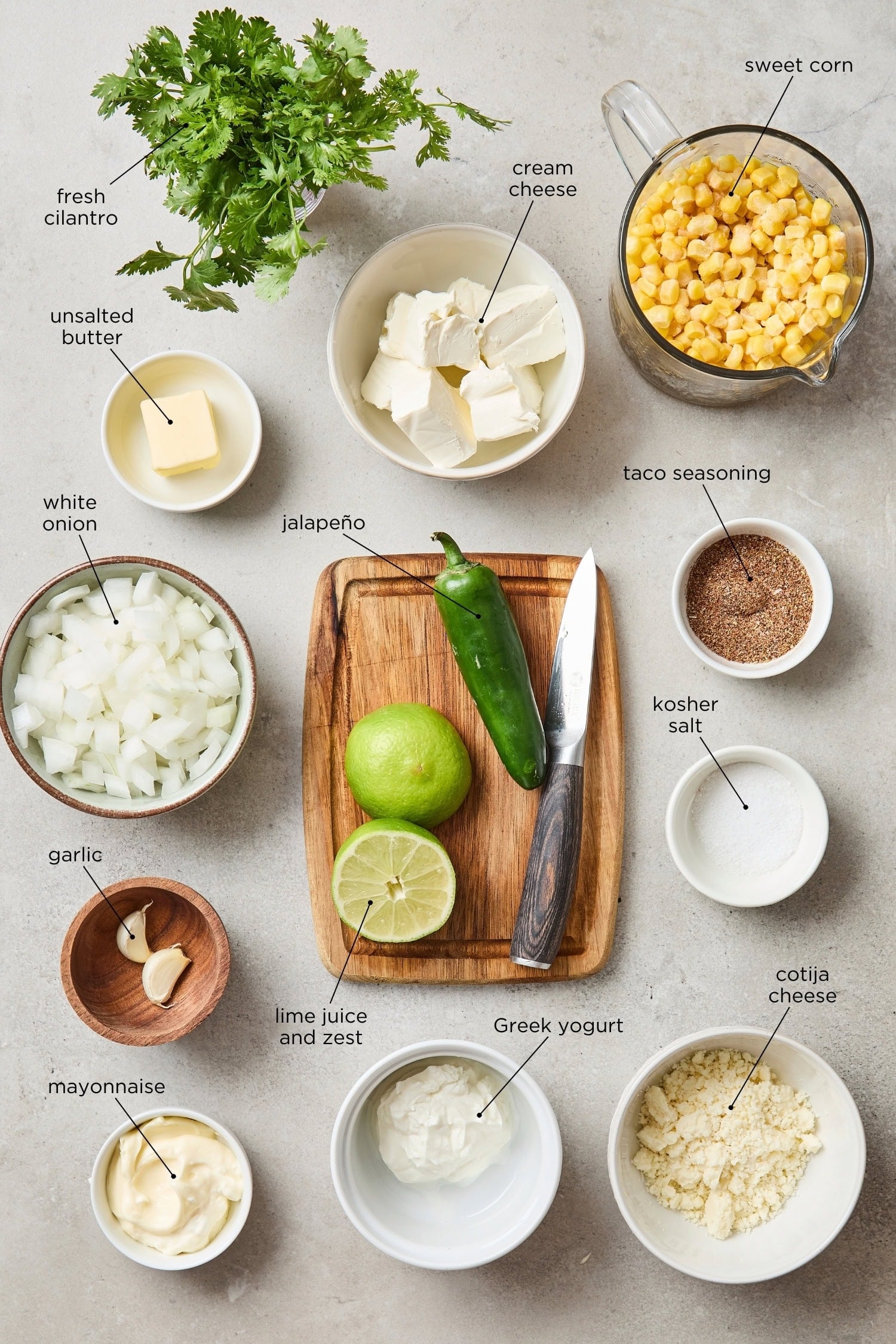 Surface filled with ingredients needed for street corn dip including sweet corn, cream cheese, yogurt, spices, and more.