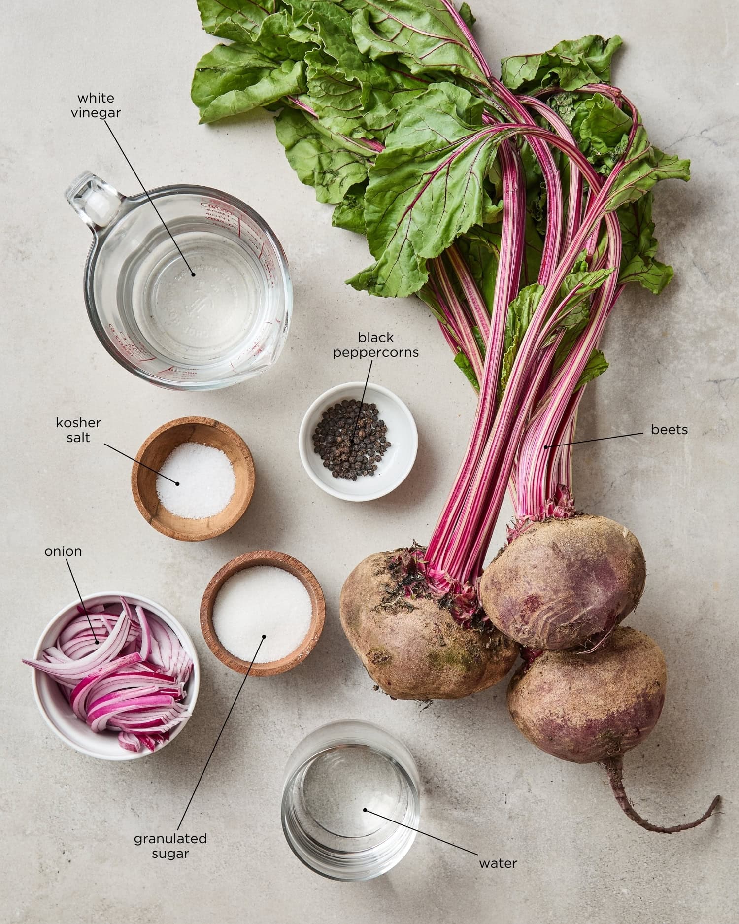 Ingredients needed for pickled beets sit on a counter including beets, vinegar, kosher salt, black peppercorn, red onion, sugar, and water.