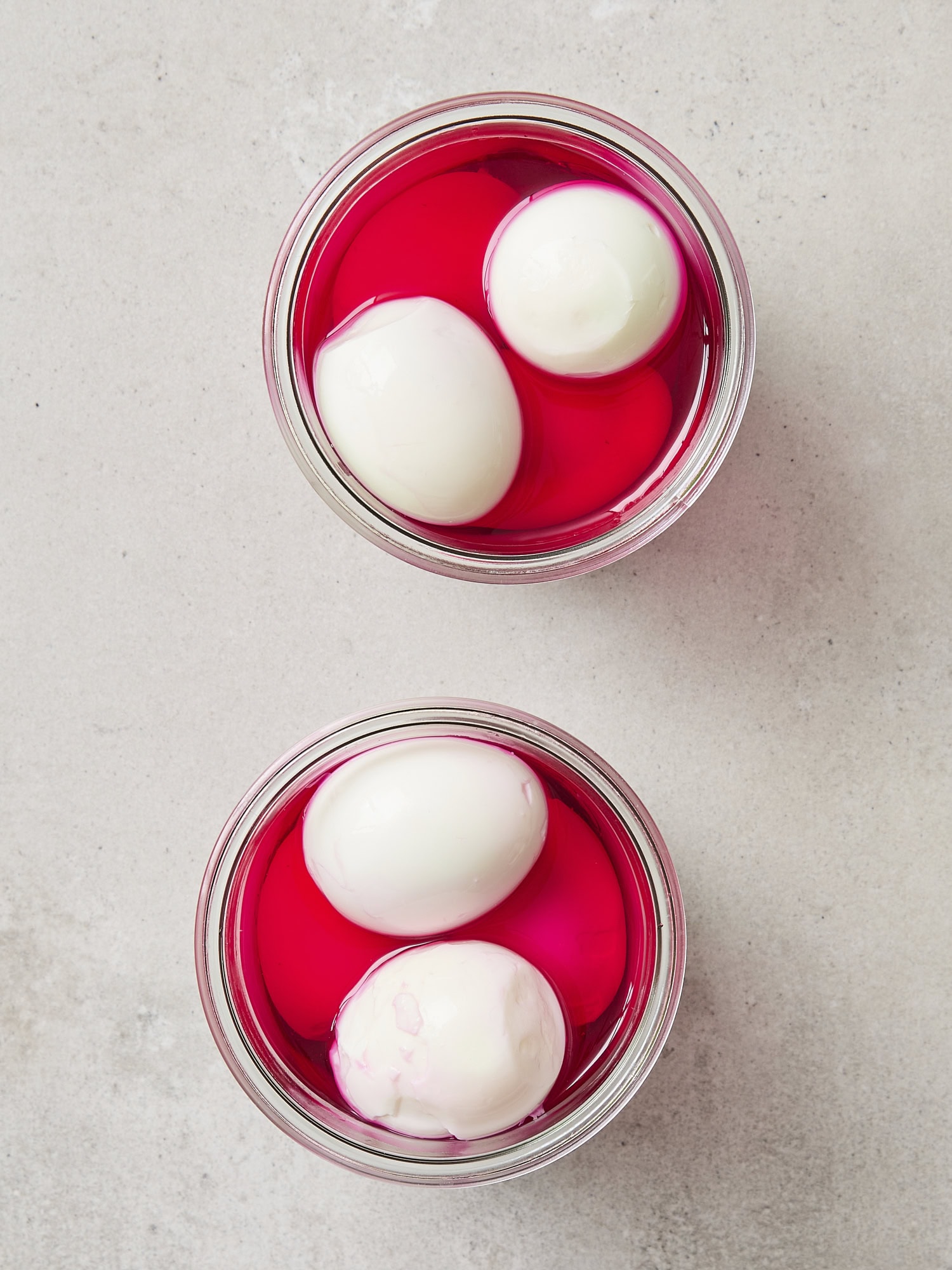 Two jars filled with hard-boiled eggs with beet brine poured on top.
