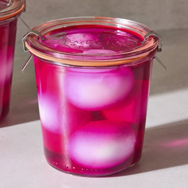 Jar filled with pickled eggs sitting in bright pink and red brine.
