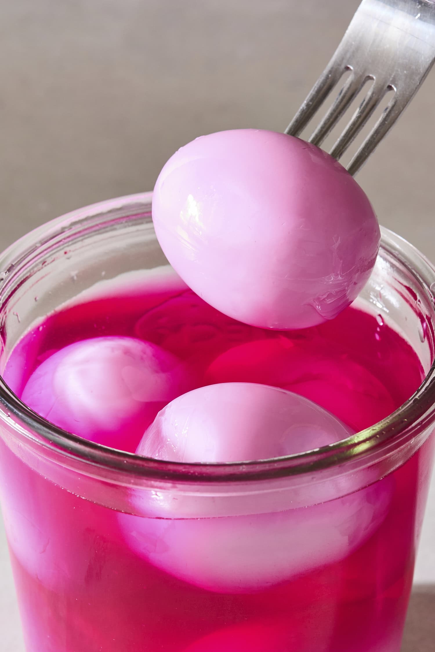 Fork with pink-colored pickled eggs being held over top of the jar filled with more eggs.