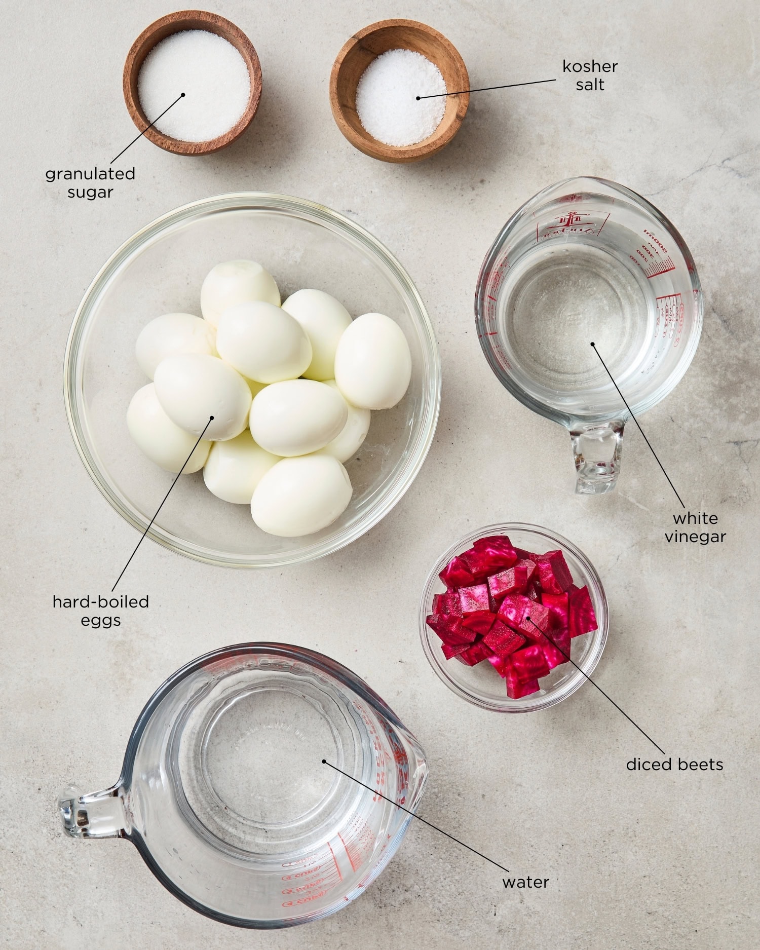 Concrete surface with ingredients needed for pickled eggs including hard-boiled eggs, beets, vinegar, and more.