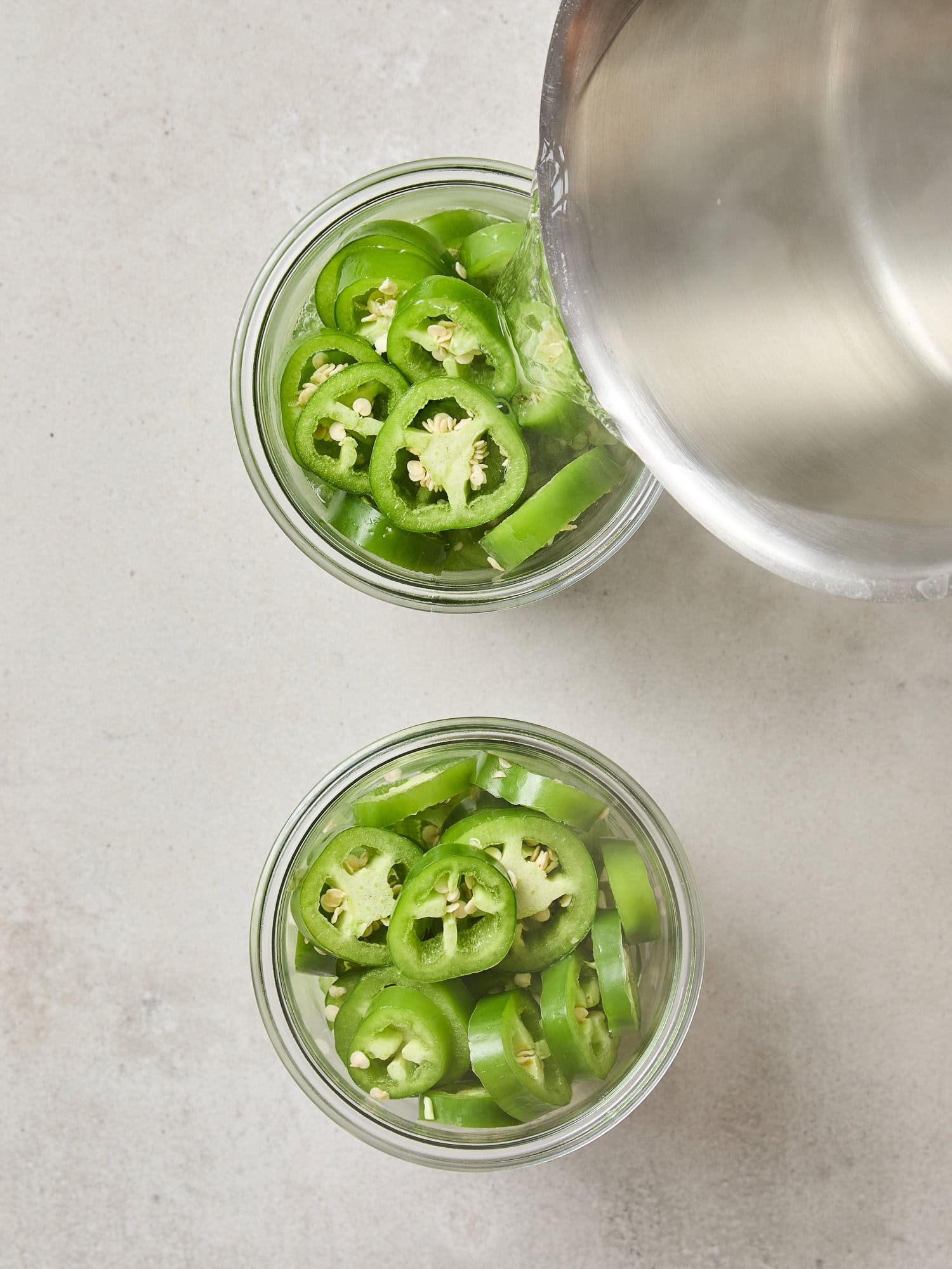 Pouring brine over sliced jalapeños in a jar.
