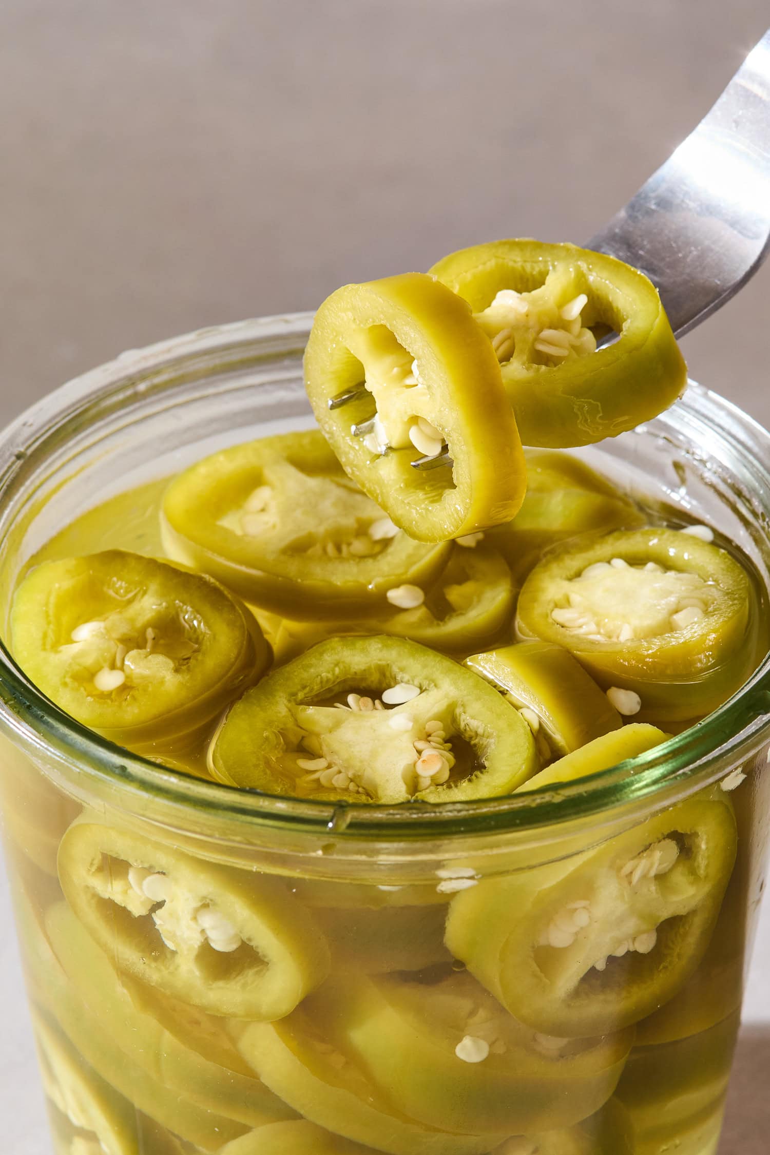 Pickled jalapeños get pulled out of a preserving jar on a fork.