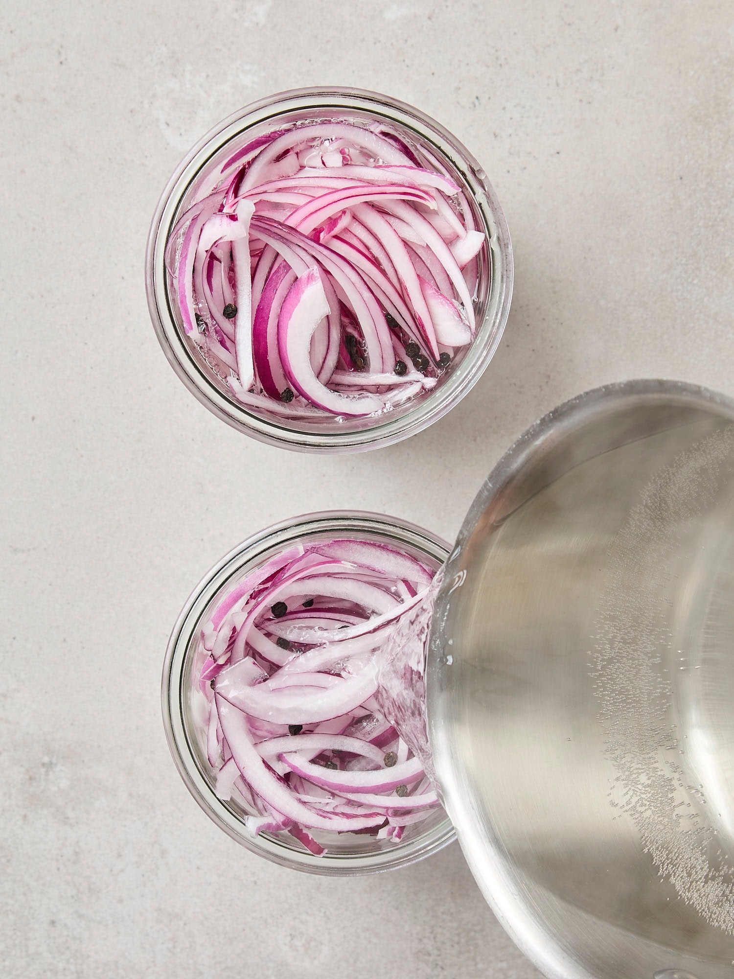 Saucepan pouring hot vinegar brine on top of sliced red onions.