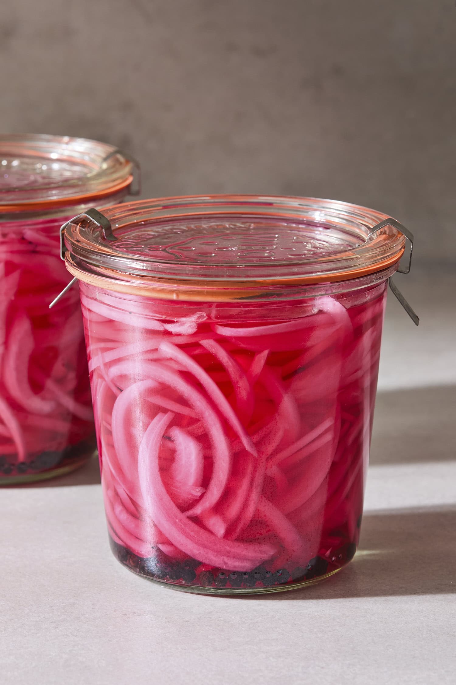 Glass jar filled with pickled red onions in bright red brine with another jar in background.