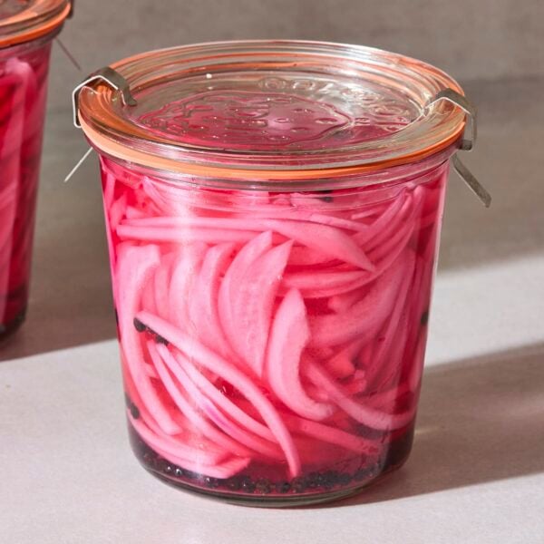Two glass jars filled with pickled red onions with bright pink liquid.
