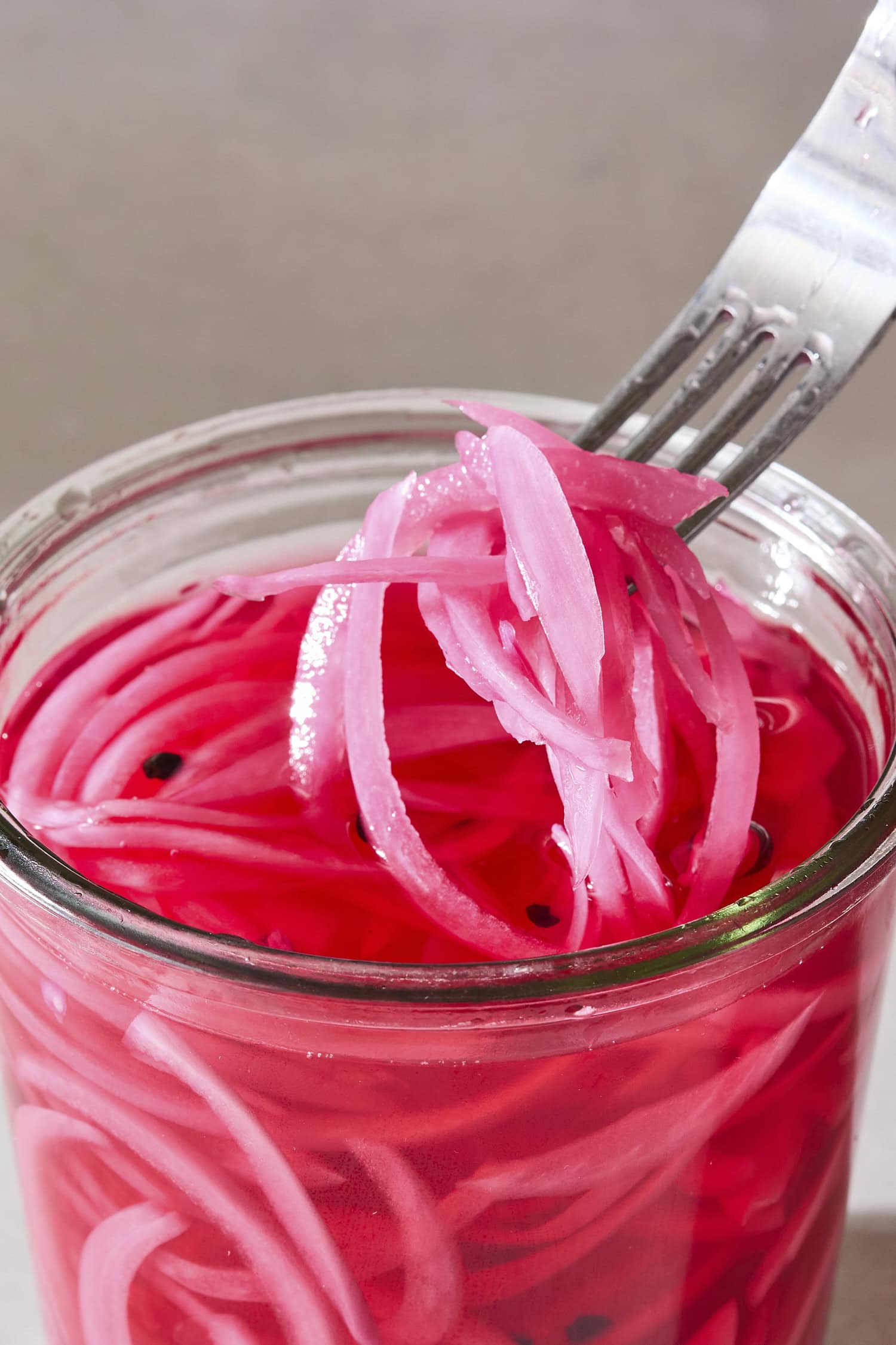 Fork lifting out a helping of pickled red onions from a jar.