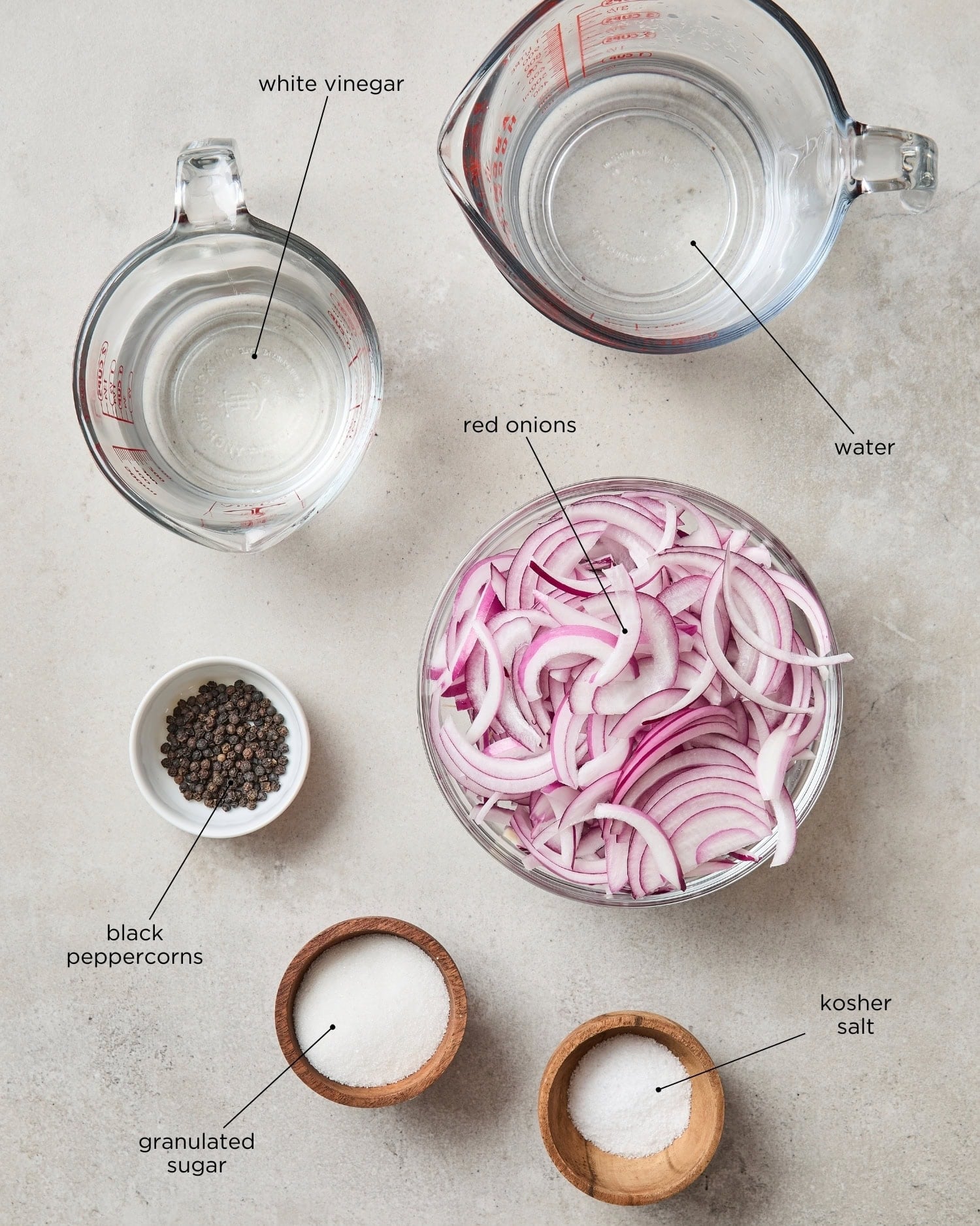 Concrete surface with ingredients for pickled red onions including water, vinegar, sugar, and more.