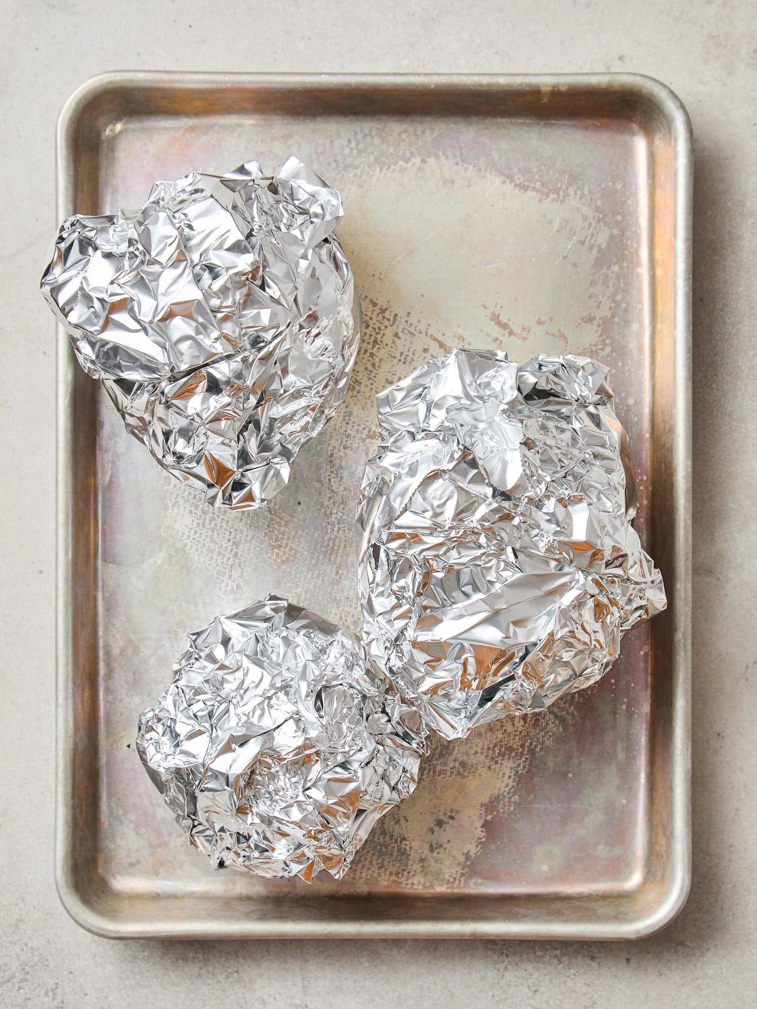 Beets wrapped in foil sit on a baking sheet prior to being cooked in the oven.