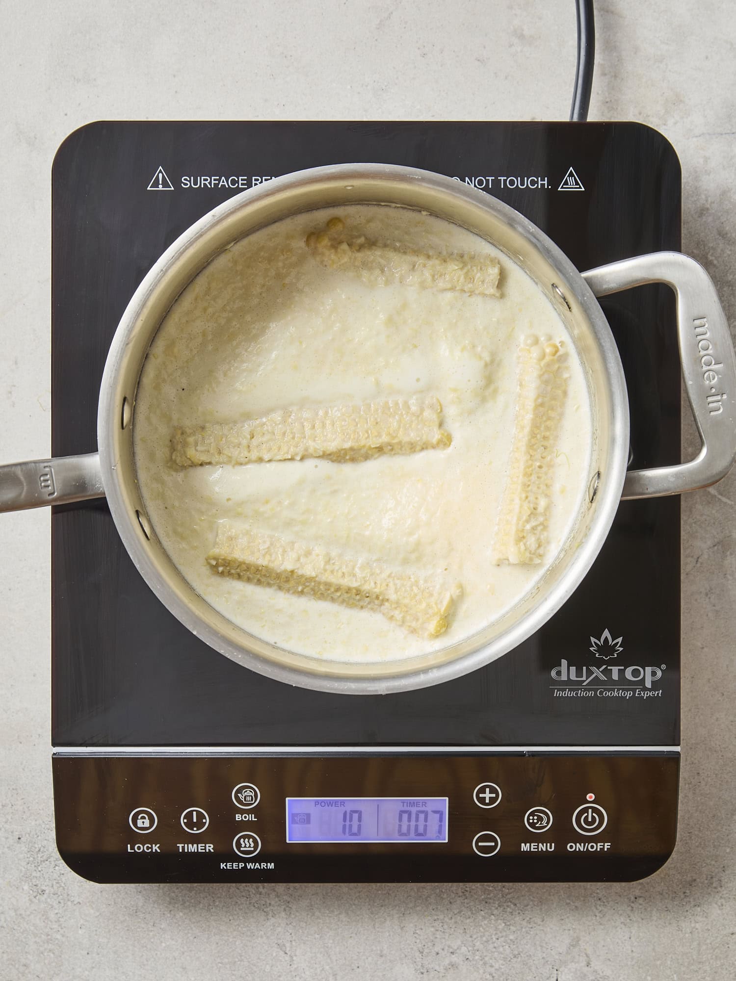 Hot plate with saucepan with milk and sweet corn cobs simmering.
