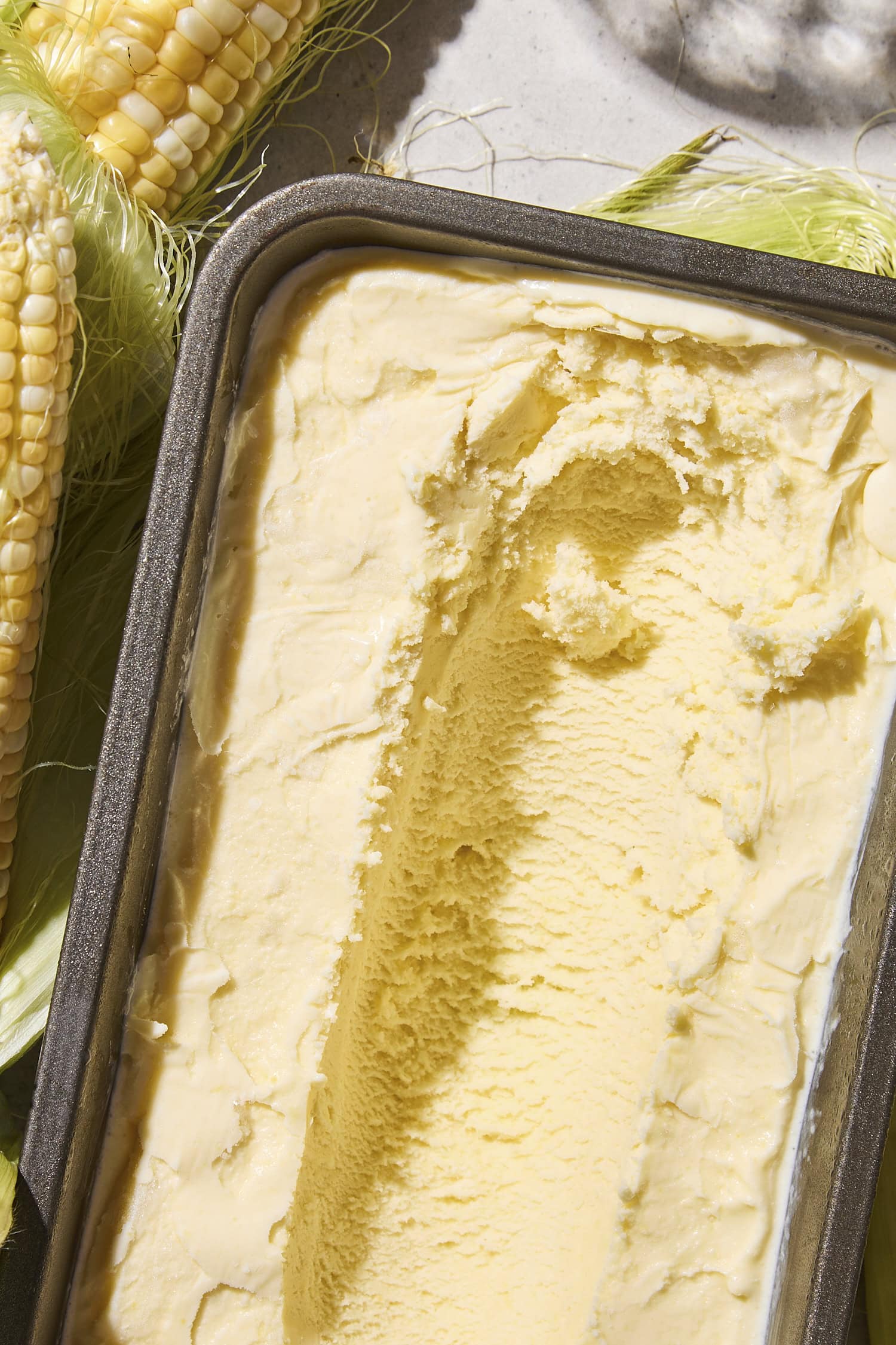 Metal container filled with sweet corn ice cream with scoop taken out showing texture.